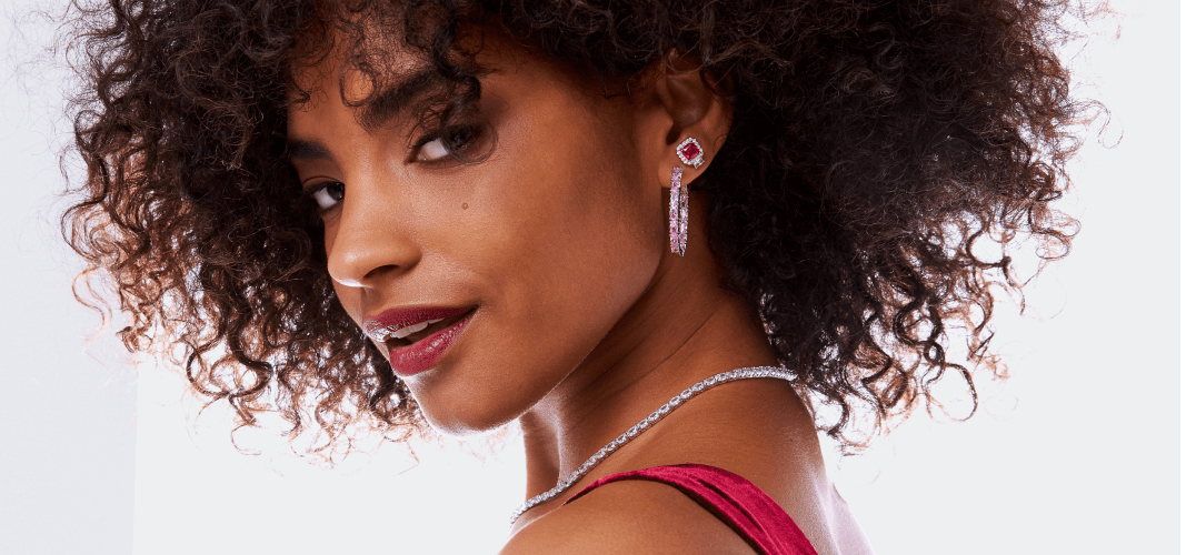 woman wearing a pink gemstone hoop and a red stud earring stacked in one ear