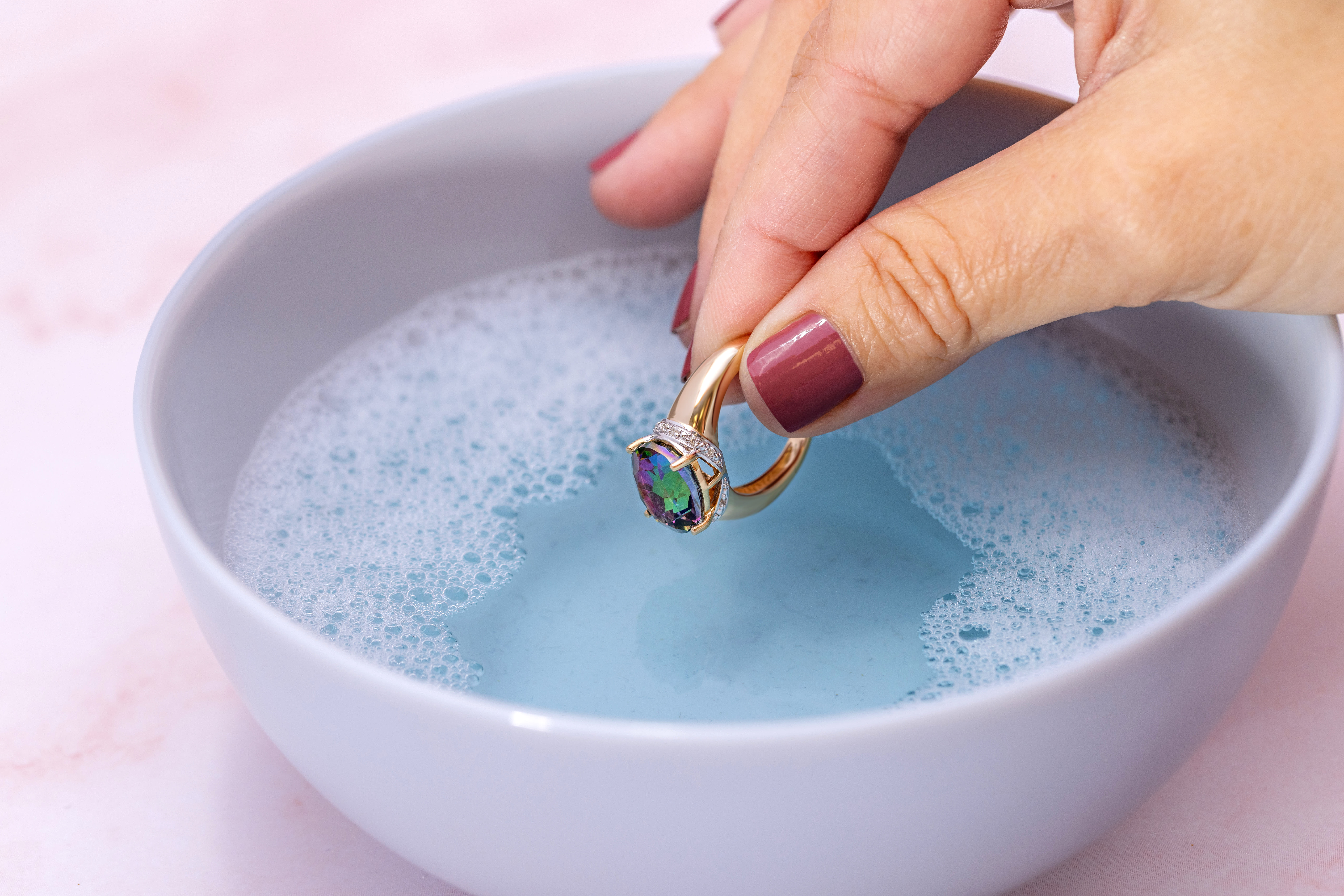 a mullticolored gemstone, gold ring being dipped in soapy water