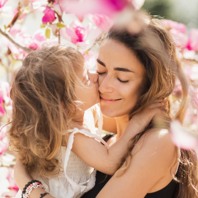 mother and daughter hugging with spring flowers behind them