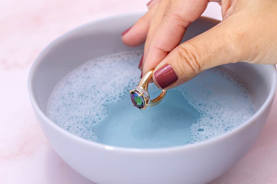 a mullticolored gemstone, gold ring being dipped in soapy water 