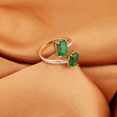 A gold ring encrusted with little diamonds and two large emerald gemstones 