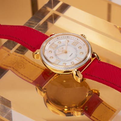 A diamond and gold watch with a vegan red leather band