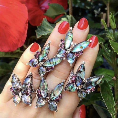 woman's hand with multiple abalone and rhodolite butterfly rings