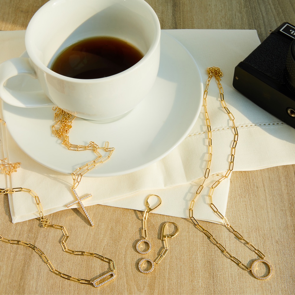 Gold chain necklaces and earrings next to a coffee cup 